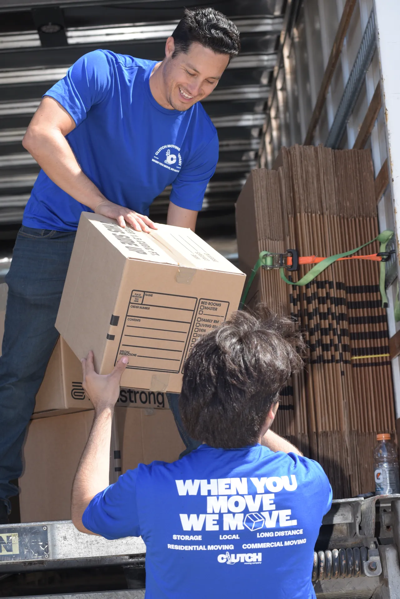 Clutch movers handing a moving box down from the truck